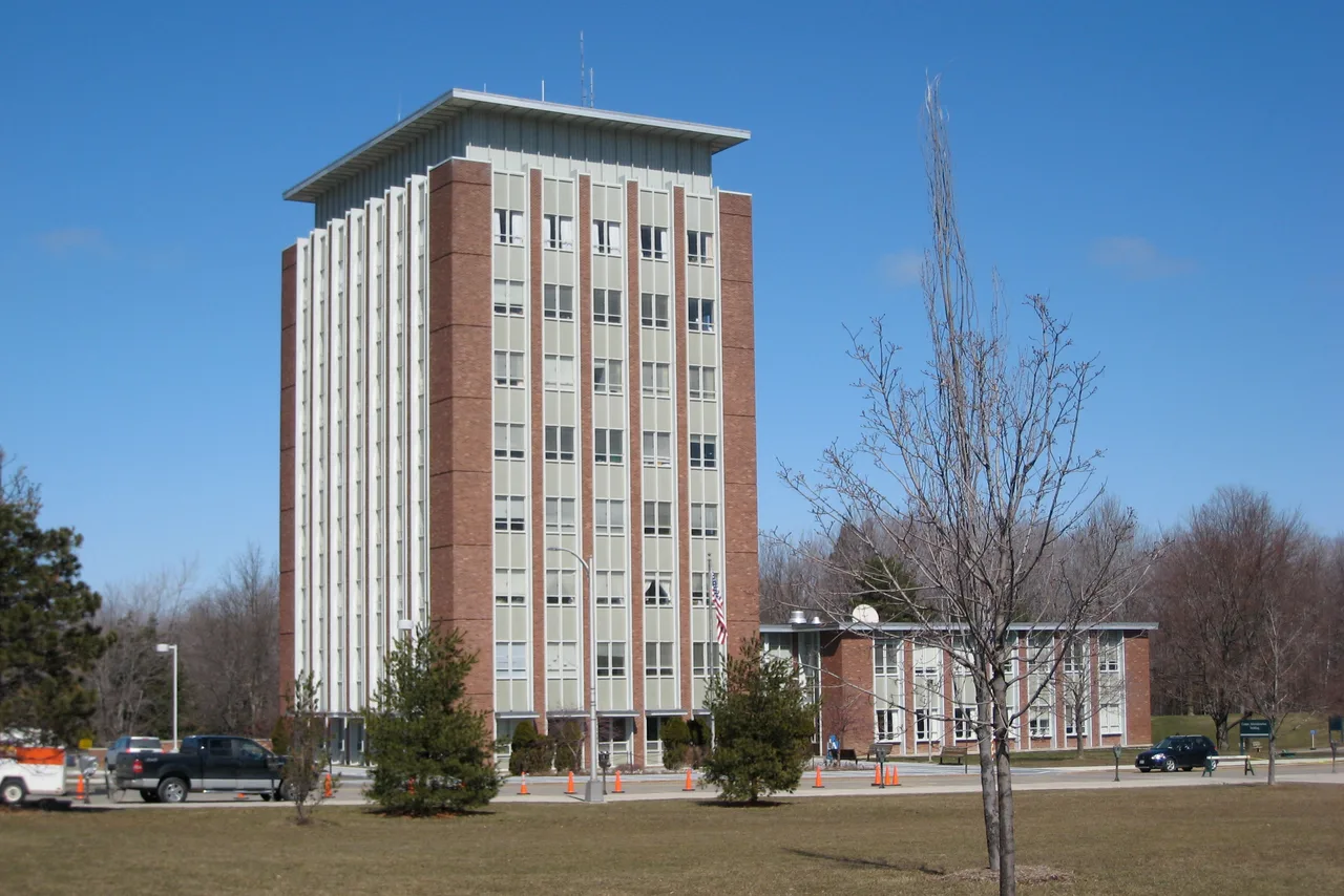 Brick-and-white Couper Administration Building tower and adjoining wing at Binghamton University, framed by campus lawn and trees.