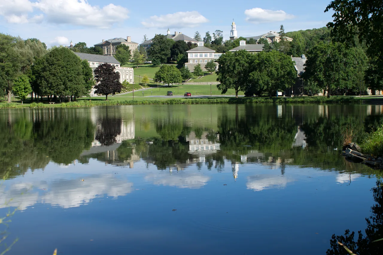 Colgate University buildings and hillside reflected across Taylor Lake.