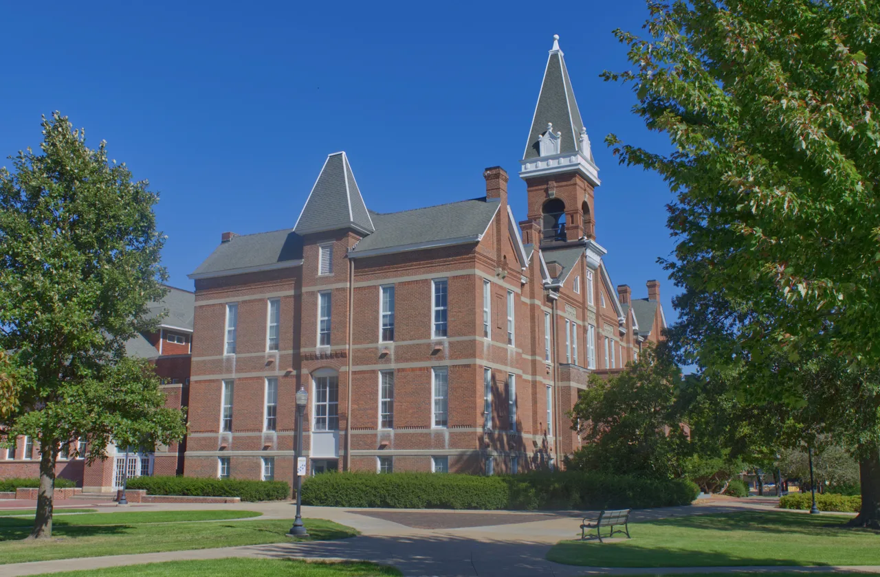 Brick exterior and tower of Old Main with lawn, trees and walking paths at Drake University.