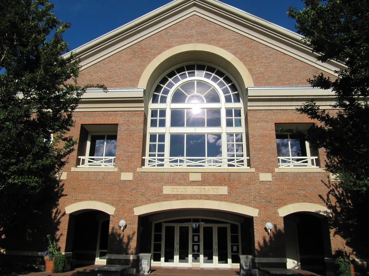 Brick Belk Library facade at Elon University, with an arched window and trees framing the entrance