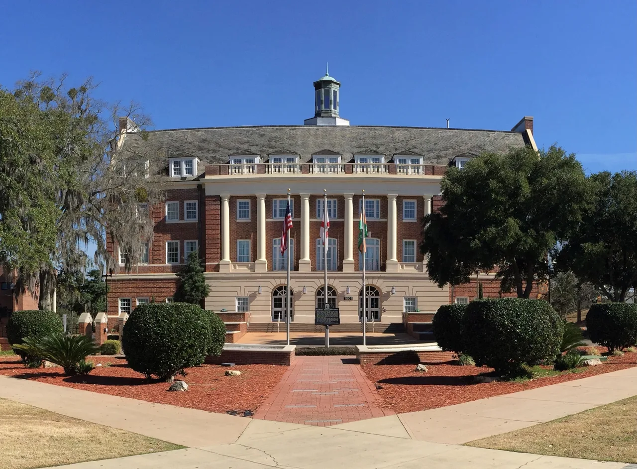 Columned brick Lee Hall facade at Florida A&M University, with flags, campus trees and landscaped paths