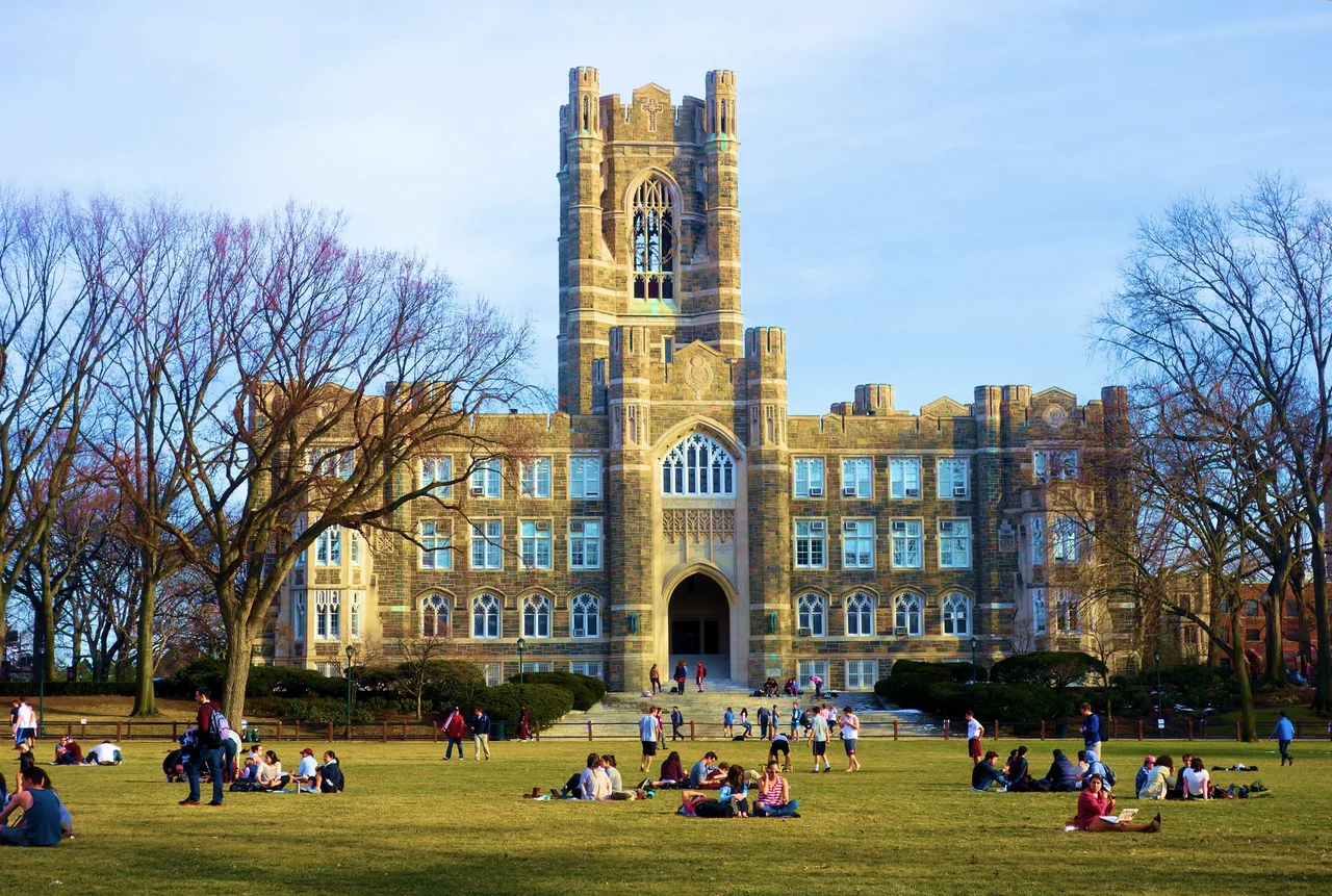 Keating Hall and its central tower at Fordham University, with trees and students on the Edwards Parade lawn
