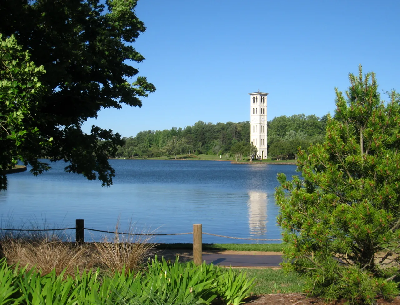 White Bell Tower reflected in the campus lake at Furman University, framed by trees and lakeside plants