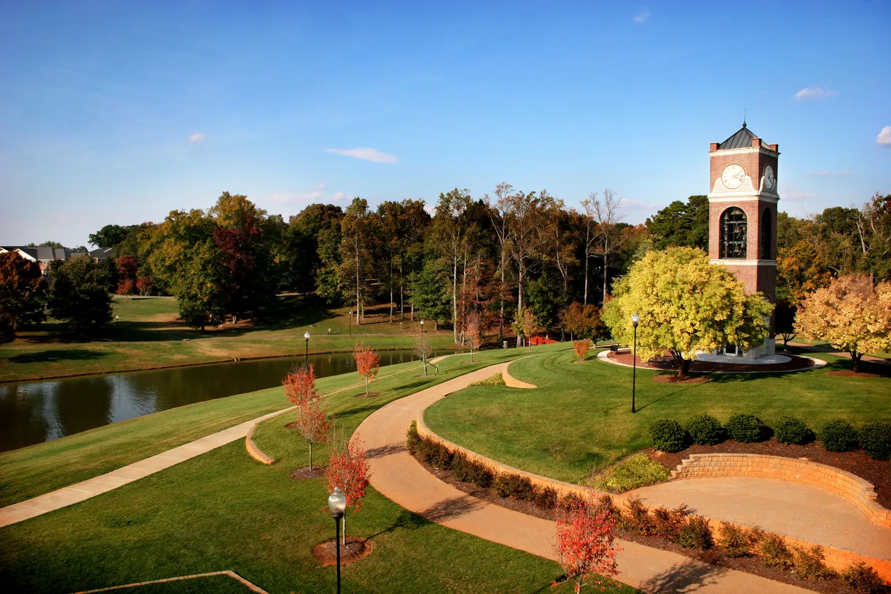 Gardner-Webb University campus lake and curved walking paths beside a brick bell tower and autumn trees