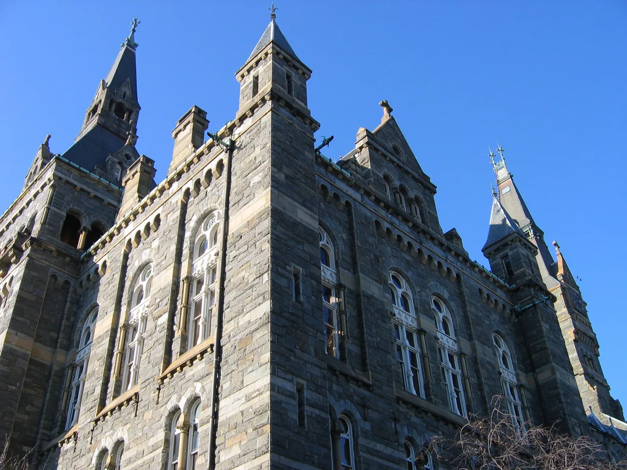 An upward view of Healy Hall’s stone facade, arched windows and towers at Georgetown University against a blue sky.