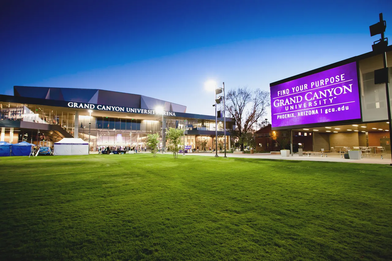 The illuminated glass exterior of Grand Canyon University Arena and adjacent university signage beyond a campus lawn at dusk in 2011.