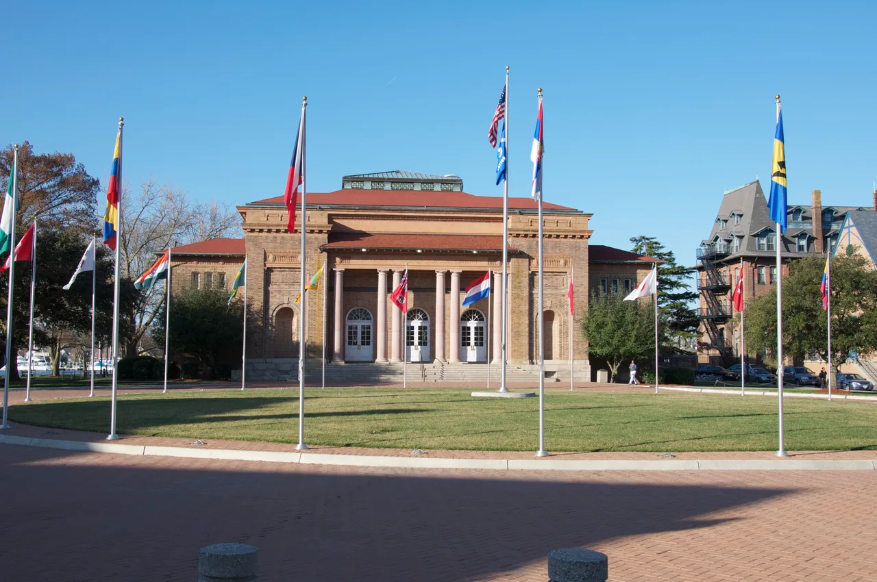 Robert C. Ogden Hall’s tan brick facade and columned entrance beyond a lawn with flagpoles at Hampton University.