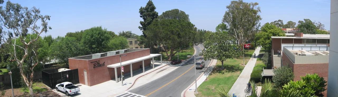 Landscaped campus paths, a road and brick buildings at California State University, Long Beach, with The Beach lettering visible on the left.