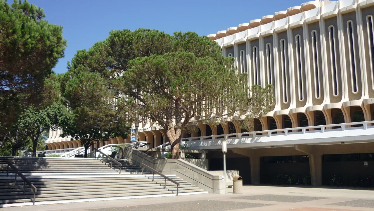 Jack Langson Library with tall vertical windows, mature trees and broad entrance steps at UC Irvine.