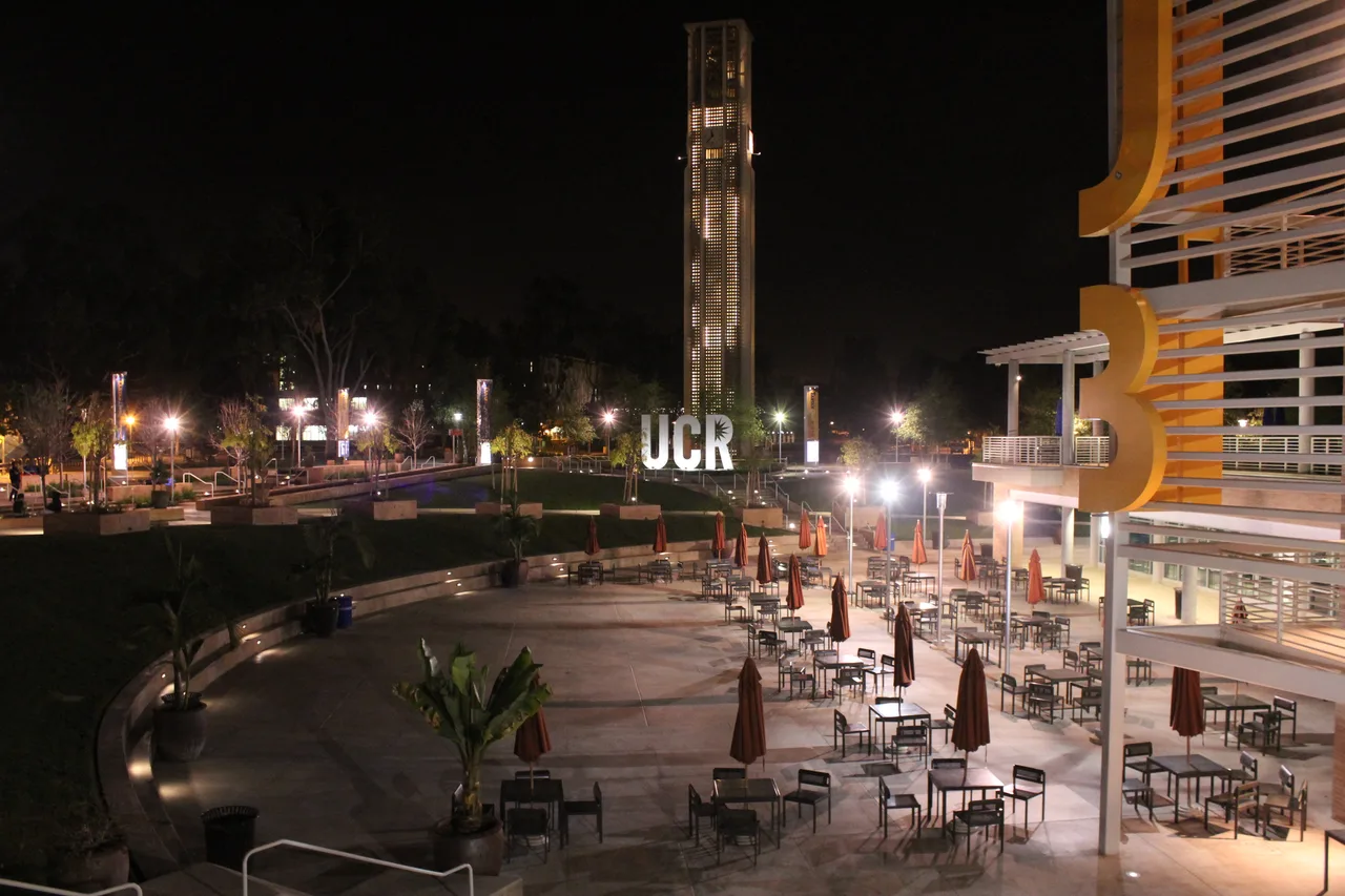 Illuminated Carillon Bell Tower above UCR letters and outdoor seating at UC Riverside at night.